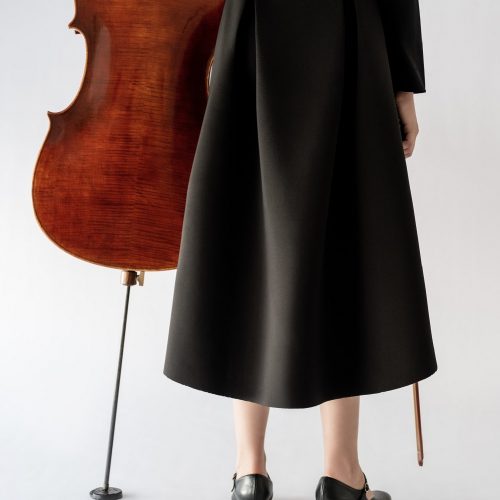 girl standing next to cello wearing black skirt back view