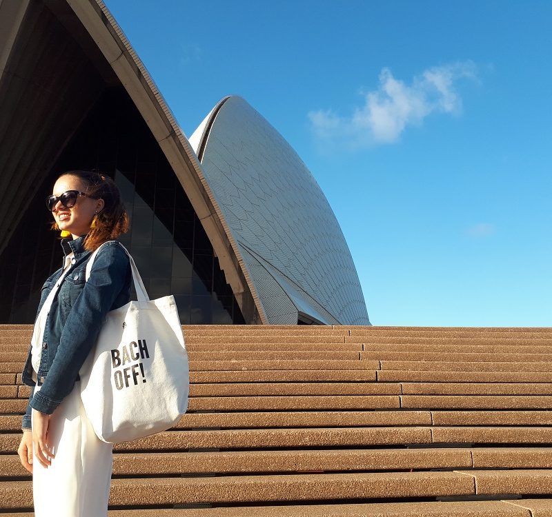 girl standing in front of opera house holding a bag